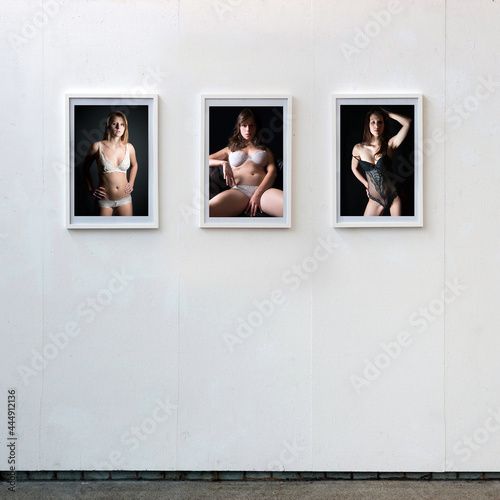 Three framed lingerie photos of beautiful young women hanging on a white wall