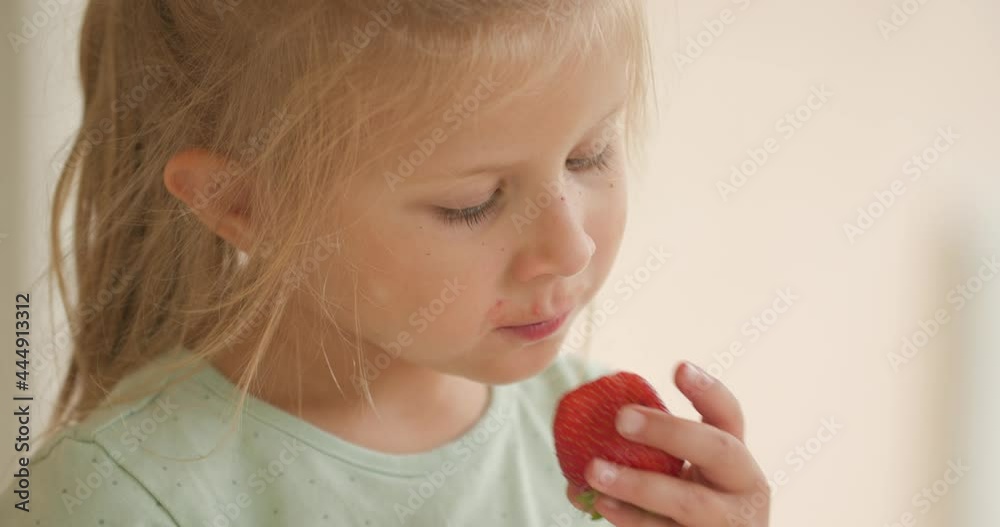 close up of cute kid in a side view position standing outside, looking away and eating strawberries close up of cute kid in a side view position standing outside, looking away and eating strawberries