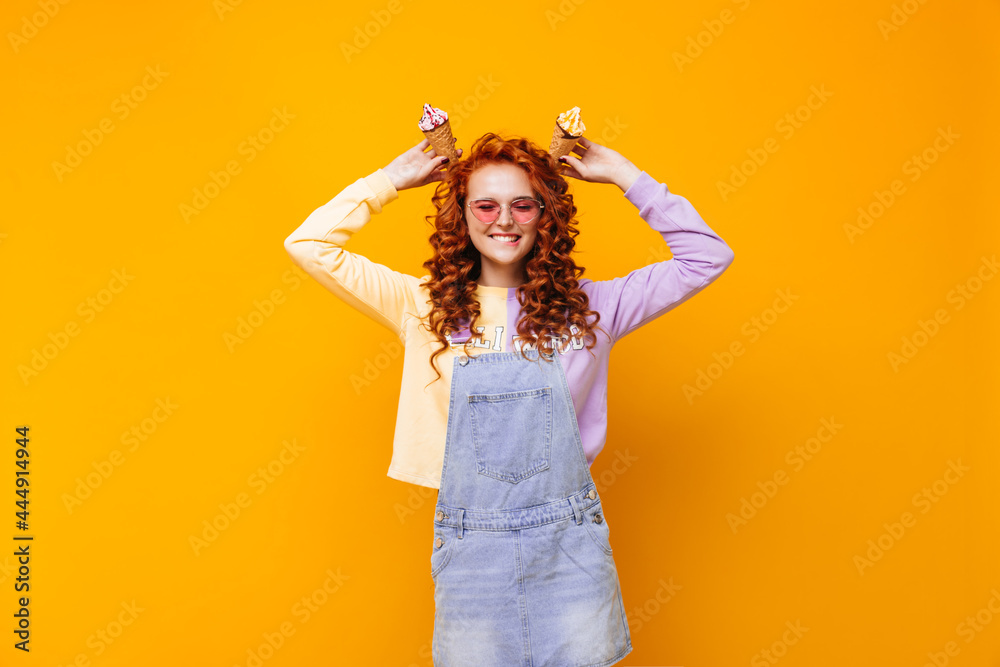 Positive woman in sundress and sweatshirt posing with ice cream on orange background Positive woman in sundress and sweatshirt posing with ice cream on orange background