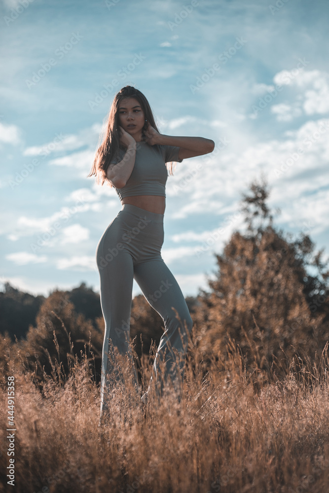 Fashion outdoor photo of beautiful woman with dark hair in luxurious sport dress posing in summer field. Fashion outdoor photo of beautiful woman with dark hair in luxurious sport dress posing in summer field.