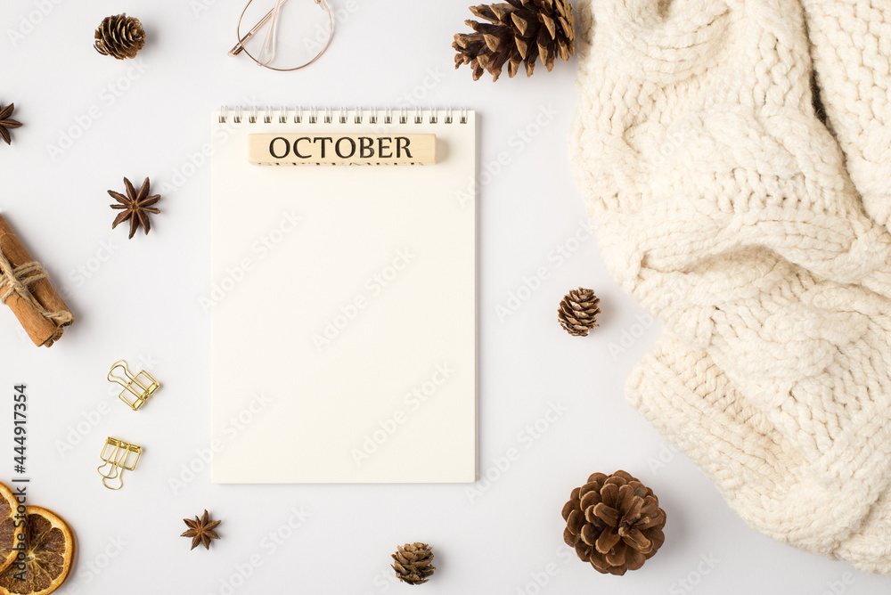 Obraz premium Top view photo of white scarf notebook with inscription october pine cones dried lemon slices cinnamon sticks golden binder clips and stylish glasses on isolated white background with blank space