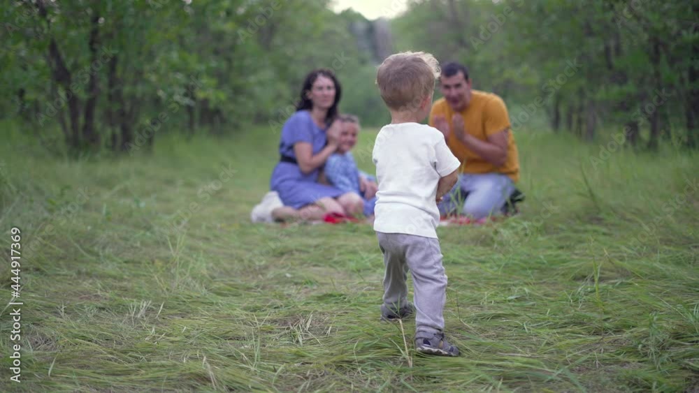 Happy family. Baby play with his parents in forest park. Family picnic on green grass in park. Baby run on green grass in forest. Happy family concept. People on picnic in park. Happy baby run Happy family. Baby play with his parents in forest park. Family picnic on green grass in park. Baby run on green grass in forest. Happy family concept. People on picnic in park. Happy baby run
