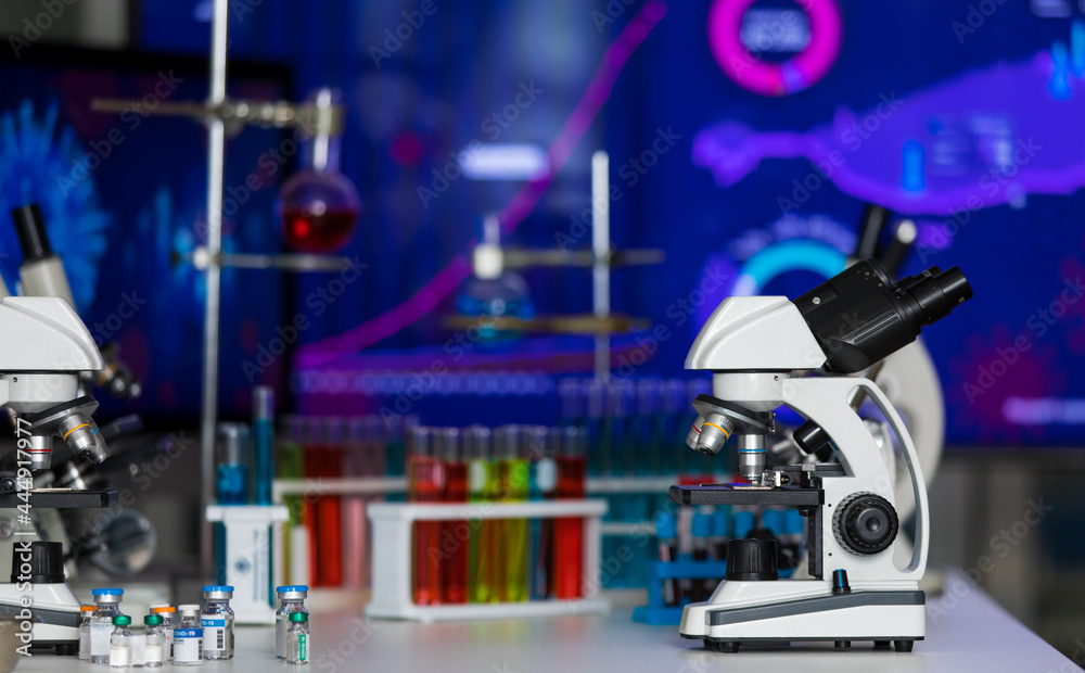 Fototapeta premium Microscope in dark laboratory with several medical tube and vial bottle for vaccine experiment and research