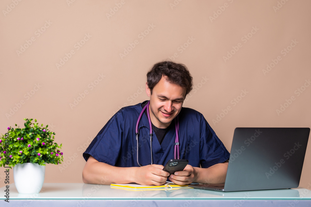 Smiling young doctor use phone at his desk in medical office Smiling young doctor use phone at his desk in medical office