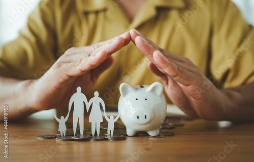 Businessman take a position to protect on the piggybank and paper family in hand, donation, saving, charity, family finance plan concept, fundraising, superannuation, financial crisis concept