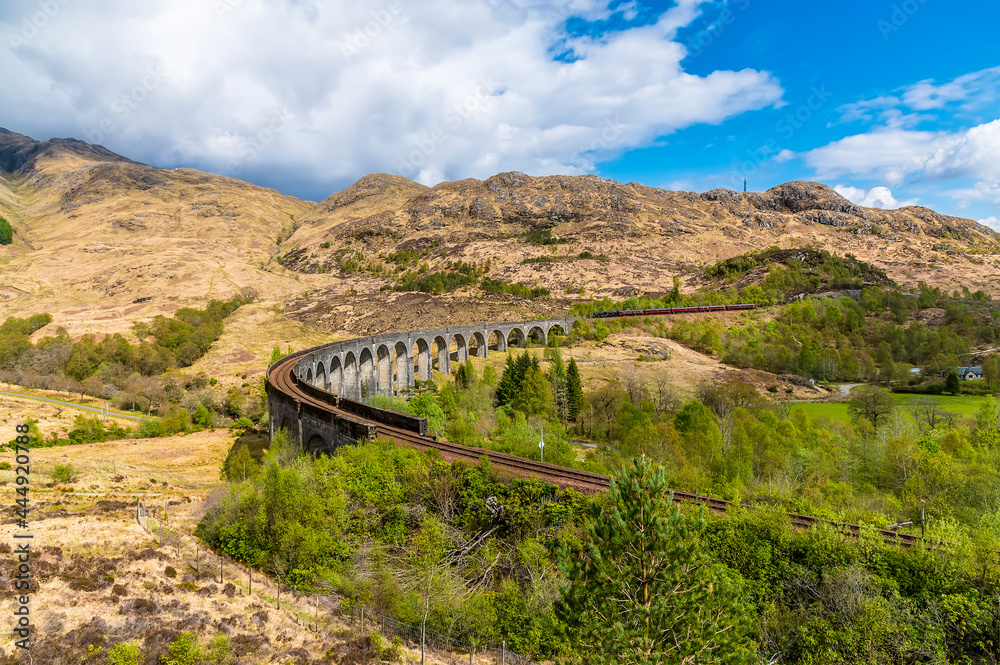 A panorama view showing the curve and a train approaching the viaduct at Glenfinnan, Scotland on a summers day