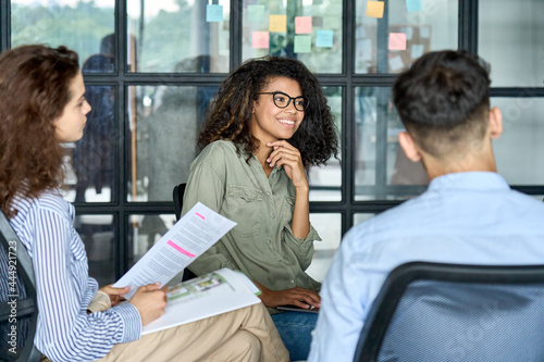 Happy young African American woman brainstorming marketing ideas about project strategy among diverse multiracial coworkers, business startup creative team or students group in office holding papers. photo