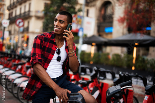 Portrait of handsome african man using electric bike in the city. Happy young man talking to the phone.