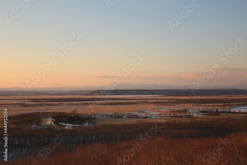 オレンジ色に染まった冬の釧路湿原向こうに雌阿寒岳が見える © Saitan