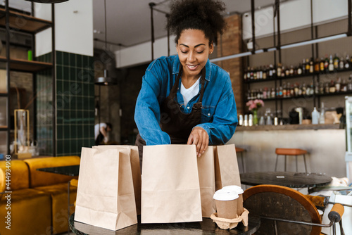 Black waitress in apron packing orders while working at cafe