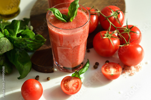 Two glasses of fresh organic tomato juice decorated with raw tomatoes and green leaves of basil on light background.Healthy diet nutrition concept.