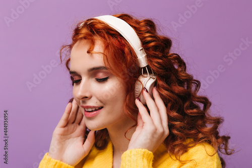 Charming girl in yellow outfit puts on headphones and listens to music on isolated background
