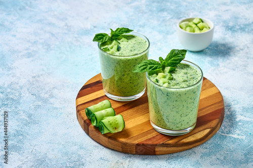 Cucumber Gazpacho - cold summer soup with basil in glasses on wooden board on light background