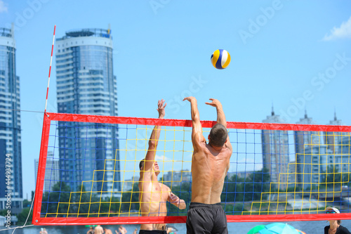 Beach volleyball. Male volley player hitting over the net attacking, another one blocking the ball