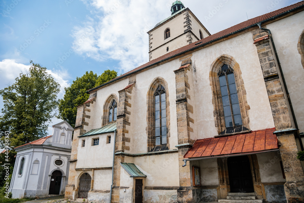 Benesov nad Ploucnici, North Bohemia, Czech Republic, 26 June 2021:  old gothic church of the Nativity of the Virgin Mary with stone towers near old saxoxy renaissance castle at summer sunny day