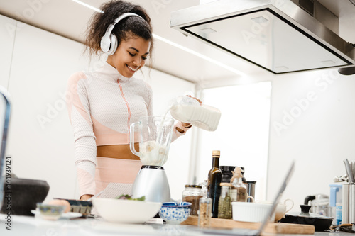 Black woman in headphones smiling and making smoothie with milk