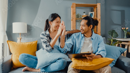 Obraz na plátně Happy asian young attractive couple man and woman sit on couch use tablet shopping online furniture decorate home in the living room at new house