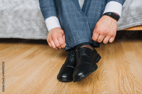 A man, a businessman, ties his shoelaces with his hands on shiny black leather shoes. Wedding portrait of the groom in the morning. Preparation for work.