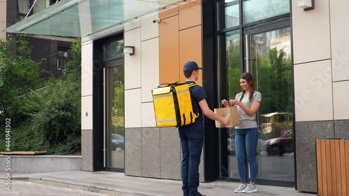 Wide shot positive food delivery man courier with yellow thermal backpack deliver order parcel to happy woman customer. Deliveryman worker delivers lunch to smiling client. Online internet shopping