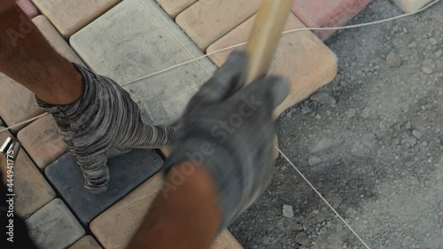 Closeup view of mason 's hands working with cobblestone . Construction worker laying paving slabs on the street. Engineer on protective gloves makes the sidewalk , hitting stone with hammer 
