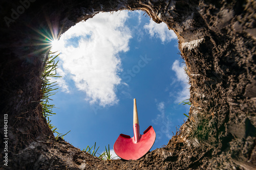 Looking up from hole in yard with shovel. Buried underground utilities, digging a hole and gardening concept photo