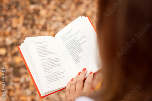 Woman reading poems in autumn park. Back view of opened book with red cover in hands of a girl. photo