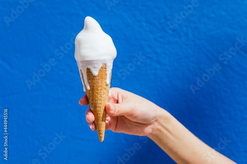 Crop woman with melting ice cream against blue wall