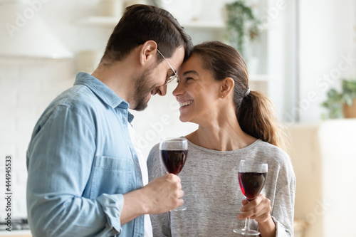 Loving young couple holding wine glasses touch foreheads relish romantic date harmonic relations celebrate life event, proposal or anniversary standing in kitchen at new own modern house. Love concept