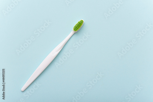 White plastic toothbrush with green bristle as flat lay. Toothbrush on blue surface, top view, space for text.