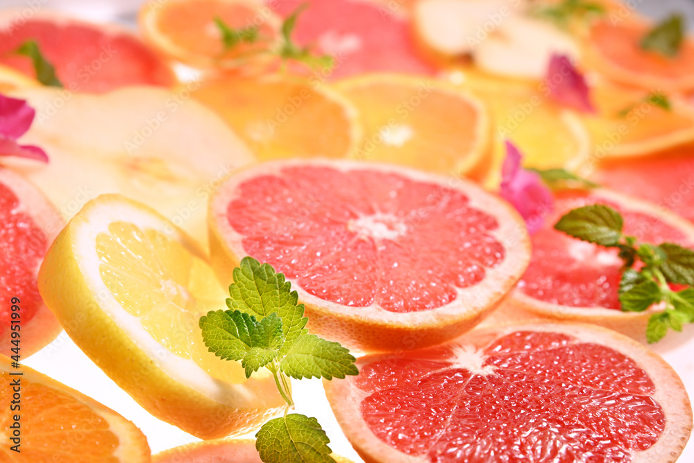citrus. Lots of sliced citrus fruits. Close-up shot with hard light. Mint petals decorate grapefruit and orange citrus. Lots of sliced citrus fruits. Close-up shot with hard light. Mint petals decorate grapefruit and orange