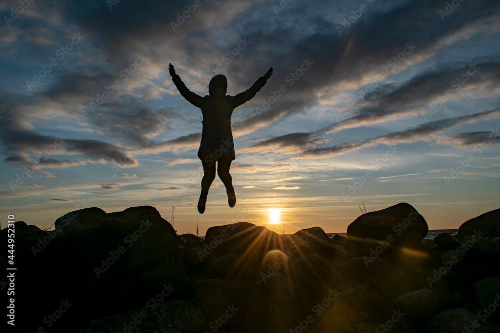 Silhouette of a young girl in a joyful jump against the background of the evening sky. World perception concept.
