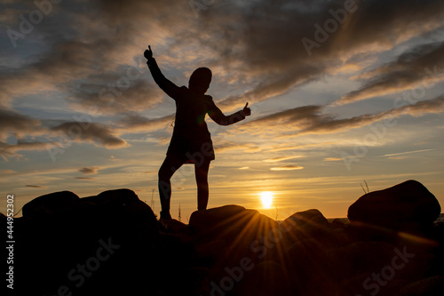 Silhouette of a young girl with a triumphantly thrown up hand against the background of the evening sky. World perception concept. © Ilia Petukhov