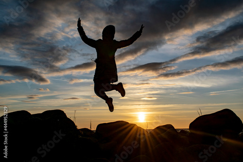 Silhouette of a young girl in a joyful jump against the background of the evening sky. World perception concept.