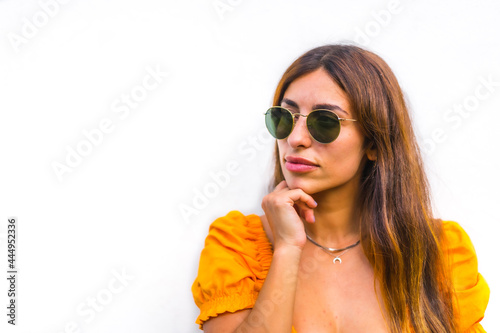 Lifestyle of a young caucasian brunette with orange t-shirt  sunglasses and short pants on a white background  with copy space and sticks. With a sweet and seductive look