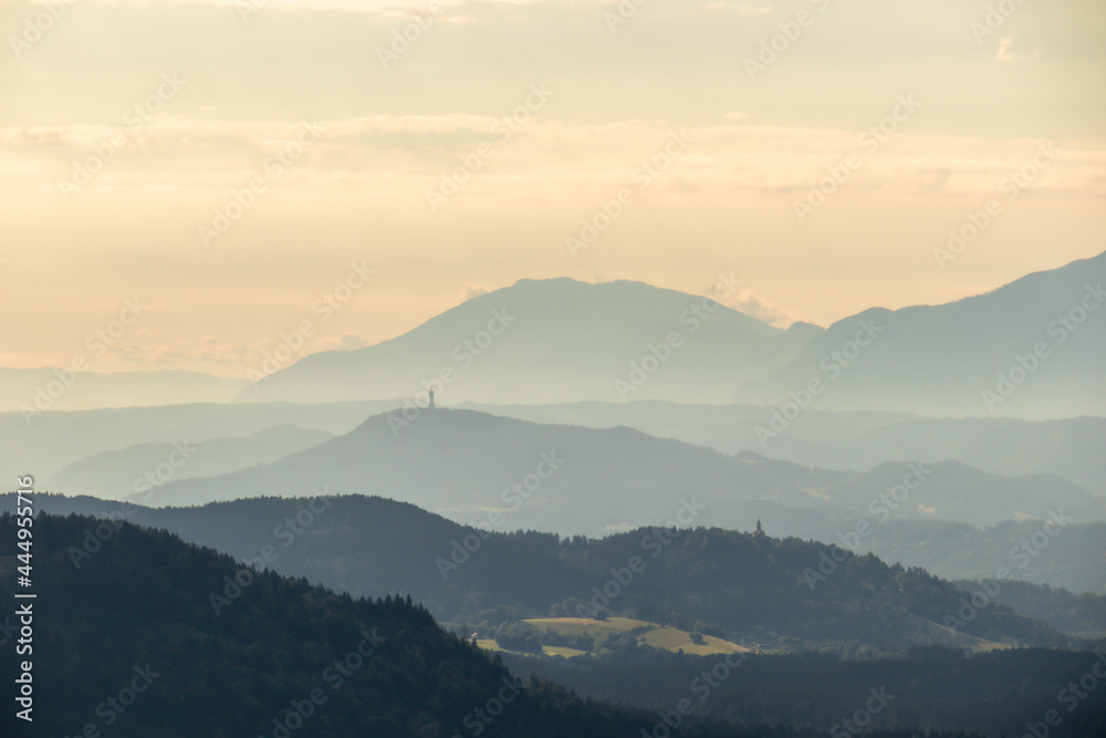 A panoramic view on endless mountain chains in Austrian Alps. The mountains are shrouded in fog. The sky is orangish and yellowish. Golden hour. Serenity and calmness