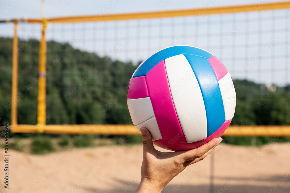 Colorful beach volleyball ball in a woman's hand. Volleyball court and net on the beach