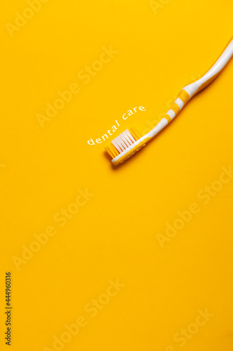 Yellow toothbrush on yellow background with the phrase "dental care" imitating toothpaste. Copy space.