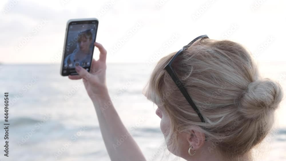 young woman taking selfie on the beach. beautiful blond woman on a holiday on the shore taking pics with her smartphone. posing to the camera creating reels for social media young woman taking selfie on the beach. beautiful blond woman on a holiday on the shore taking pics with her smartphone. posing to the camera creating reels for social media