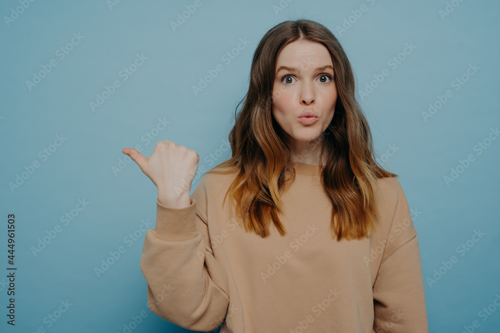 Surprised young woman pointing at copy space with wow expression Surprised young woman pointing at copy space with wow expression