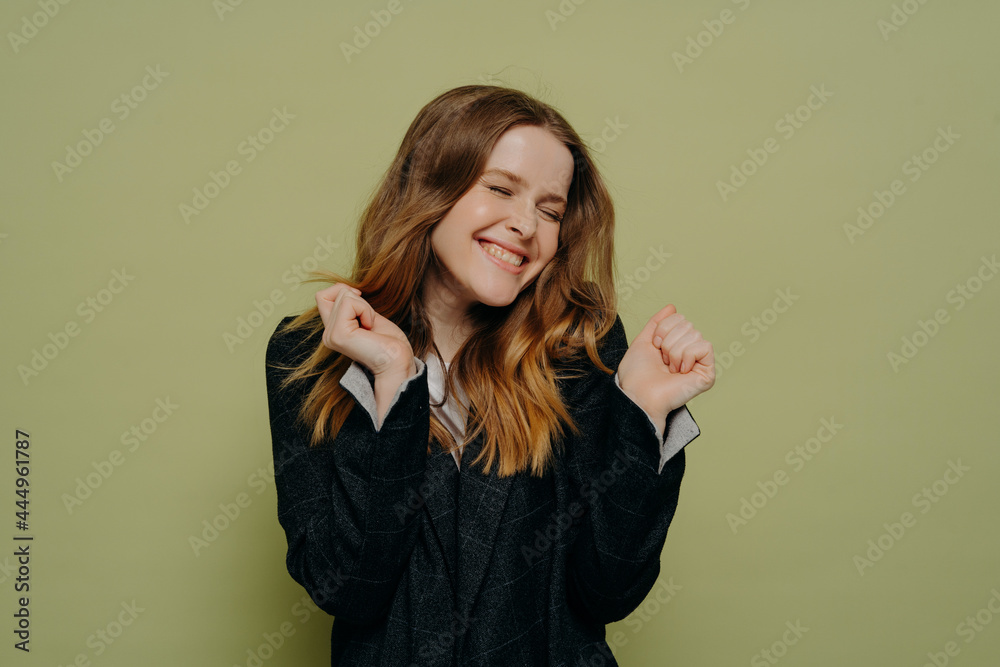 Happy young woman with closed eyes holding hands up with excitement Happy young woman with closed eyes holding hands up with excitement