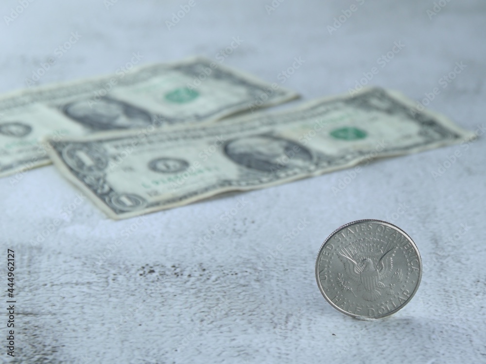 A half dollar coin, resting on a white cement floor. along with two 1 dollar bills A half dollar coin, resting on a white cement floor. along with two 1 dollar bills