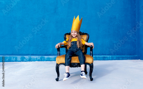 Cheerful teenager in paper crown sitting on throne