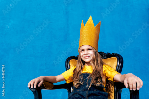 Cheerful teenager in paper crown sitting on throne