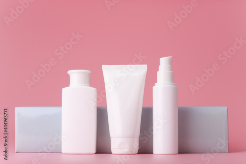 Set of white cosmetic tubes with skin care products for daily use against elegant grey wall on pink background. Cleansing foam, face scrub and cream or lotion, concept of premium beauty treatment 