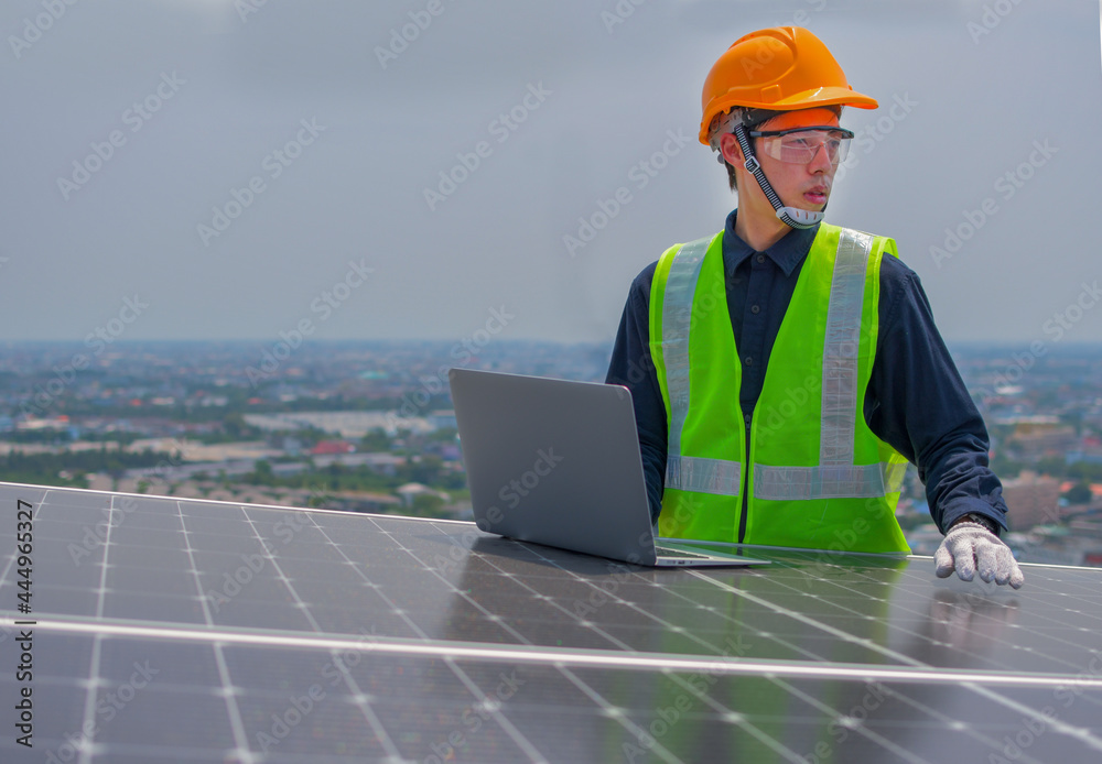 An engineer who works on the inspection and maintenance of equipment at roof-mounted solar power plants of condominium buildings, houses with a Labtop in his hand.