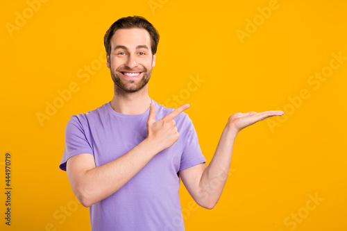 Photo of reliable guy hold palm direct finger empty space wear purple t-shirt isolated yellow color background