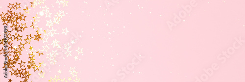 Banner with trendy gold colored stars confetti on a pink background with copyspace.