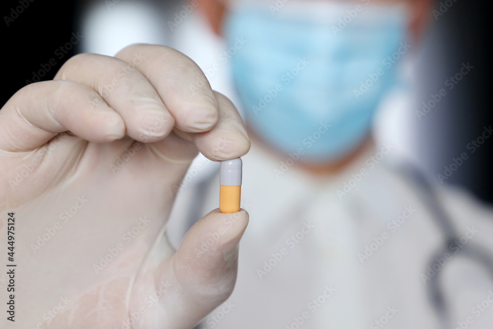 Doctor in medical mask holding pill, male hand in latex glove with medication in capsule close up. Concept of pharmacist, drugs, antibiotics or vitamins Doctor in medical mask holding pill, male hand in latex glove with medication in capsule close up. Concept of pharmacist, drugs, antibiotics or vitamins