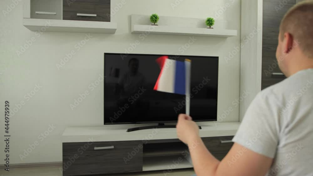 Sport fan sits at home in front of TV, he waves flag of France and celebrates victory of national team on Summer Winter games event competition. Man watches broadcast of world championship cup. Win Sport fan sits at home in front of TV, he waves flag of France and celebrates victory of national team on Summer Winter games event competition. Man watches broadcast of world championship cup. Win