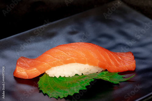 Traditional japanese nigiri sushi with salmon placed between chopsticks, separated on black background.